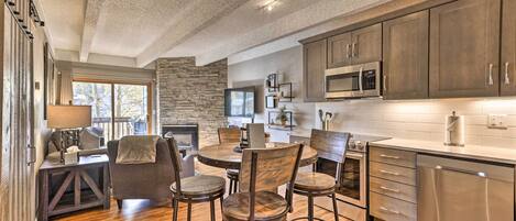 A modern kitchen with wooden flooring, a stone accent wall, and stainless steel appliances.