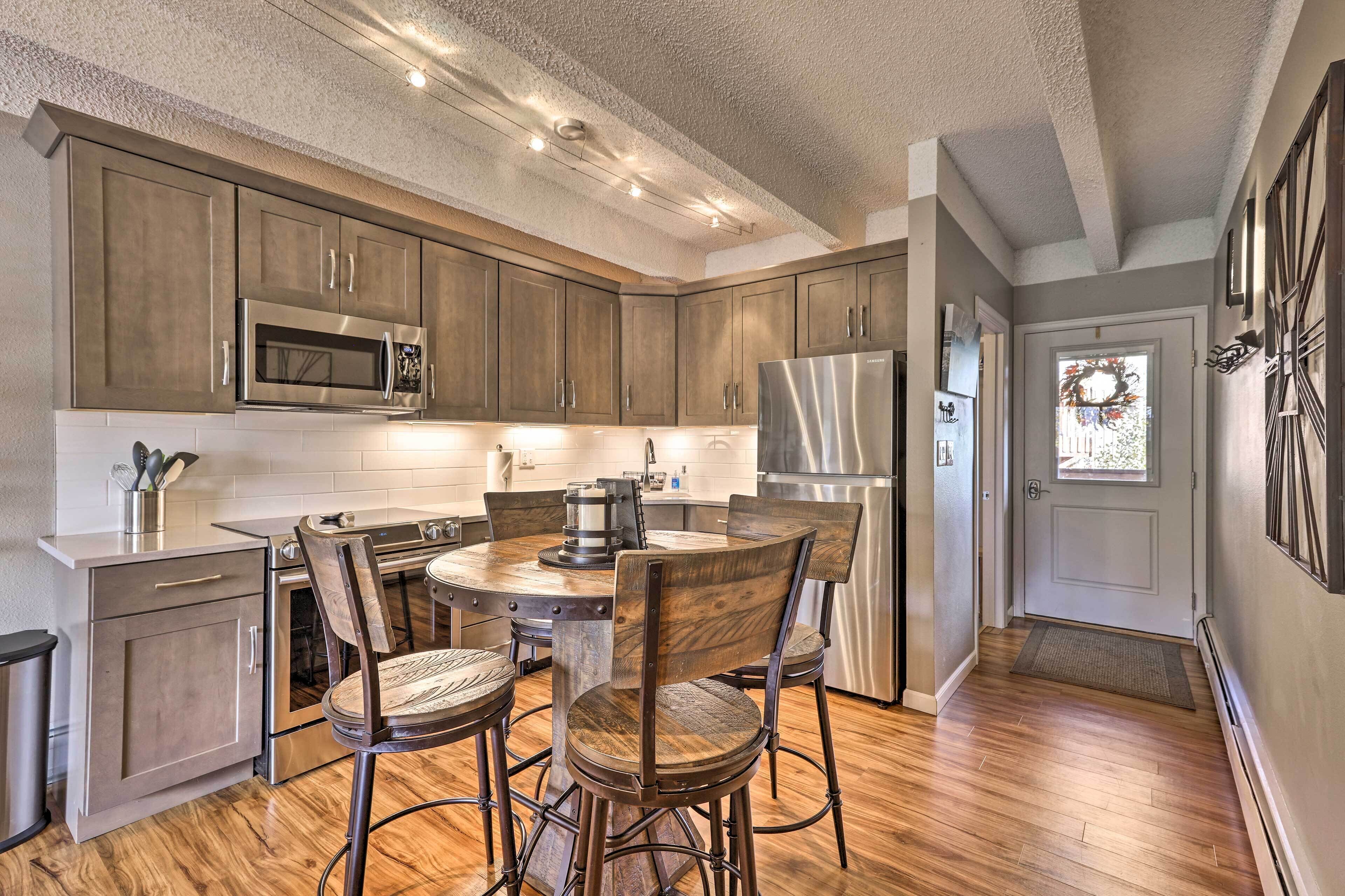 A modern kitchen with wooden cabinets, stainless steel appliances, and a dining area with metal chairs.
