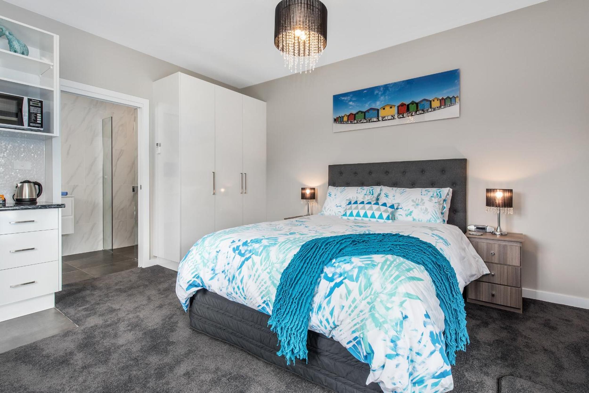 A modern bedroom with a large bed, bedside lamps, a painting on the wall, and a wardrobe.