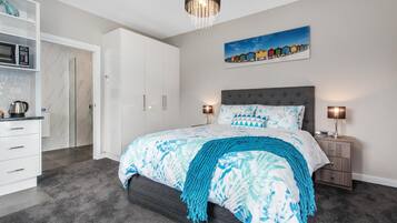 A modern bedroom with a large bed, bedside lamps, a painting on the wall, and a wardrobe.