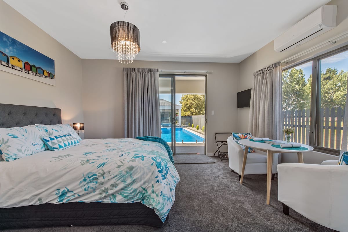A bedroom with a large bed, a desk, and a view of a swimming pool.