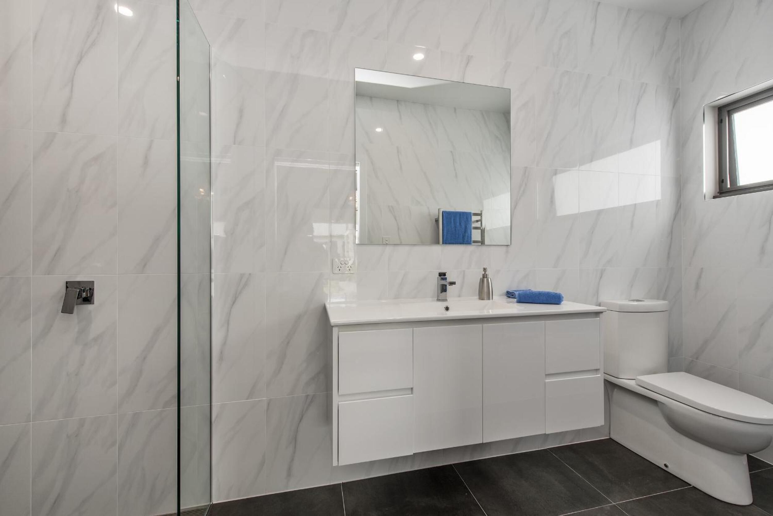 A modern bathroom with a glass shower enclosure, a white vanity with a mirror, and a toilet.