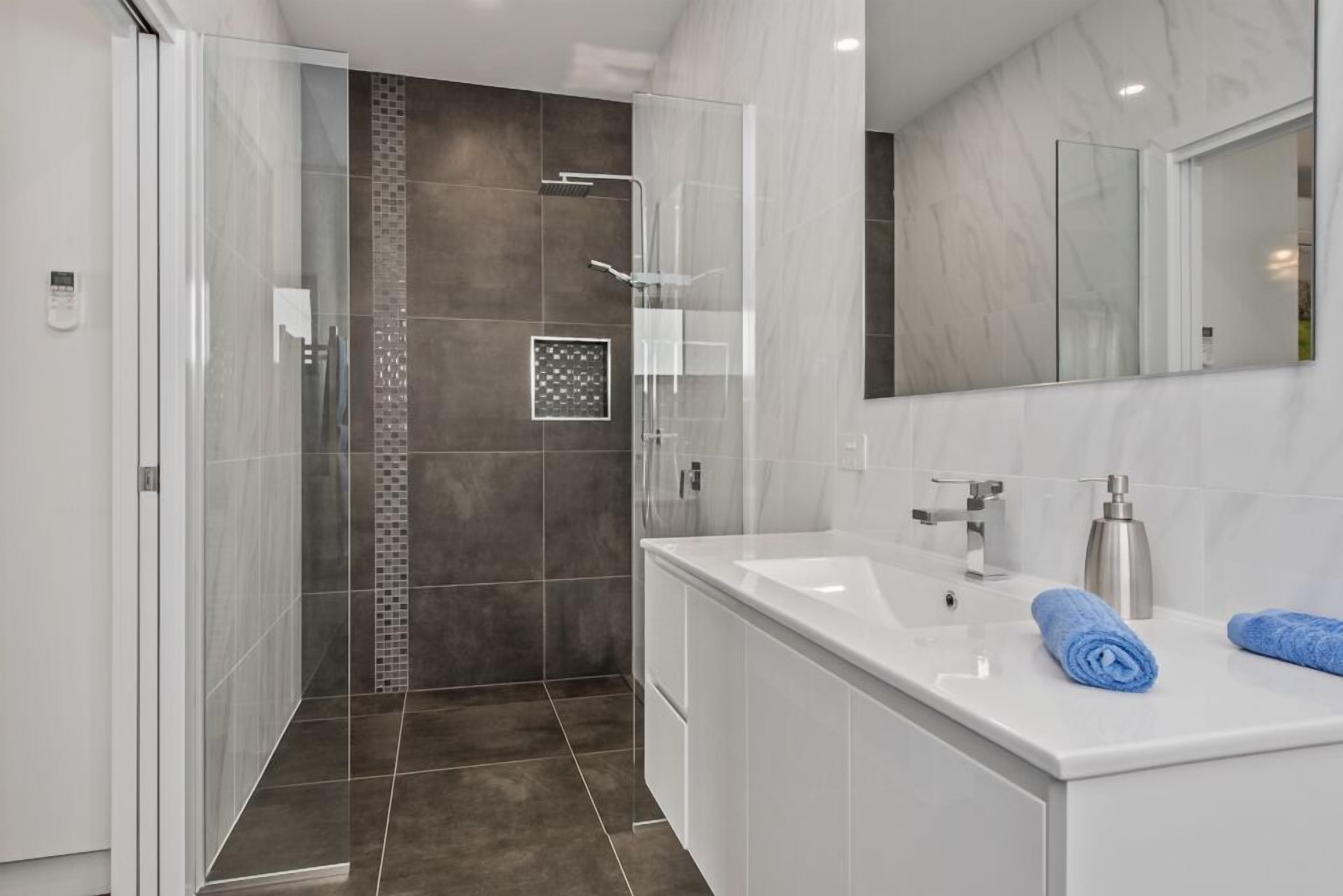 A modern bathroom with a walk-in shower, a large mirror, and a white vanity with a sink and towel.