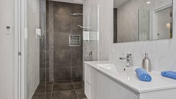 A modern bathroom with a walk-in shower, a large mirror, and a white vanity with a sink and towel.