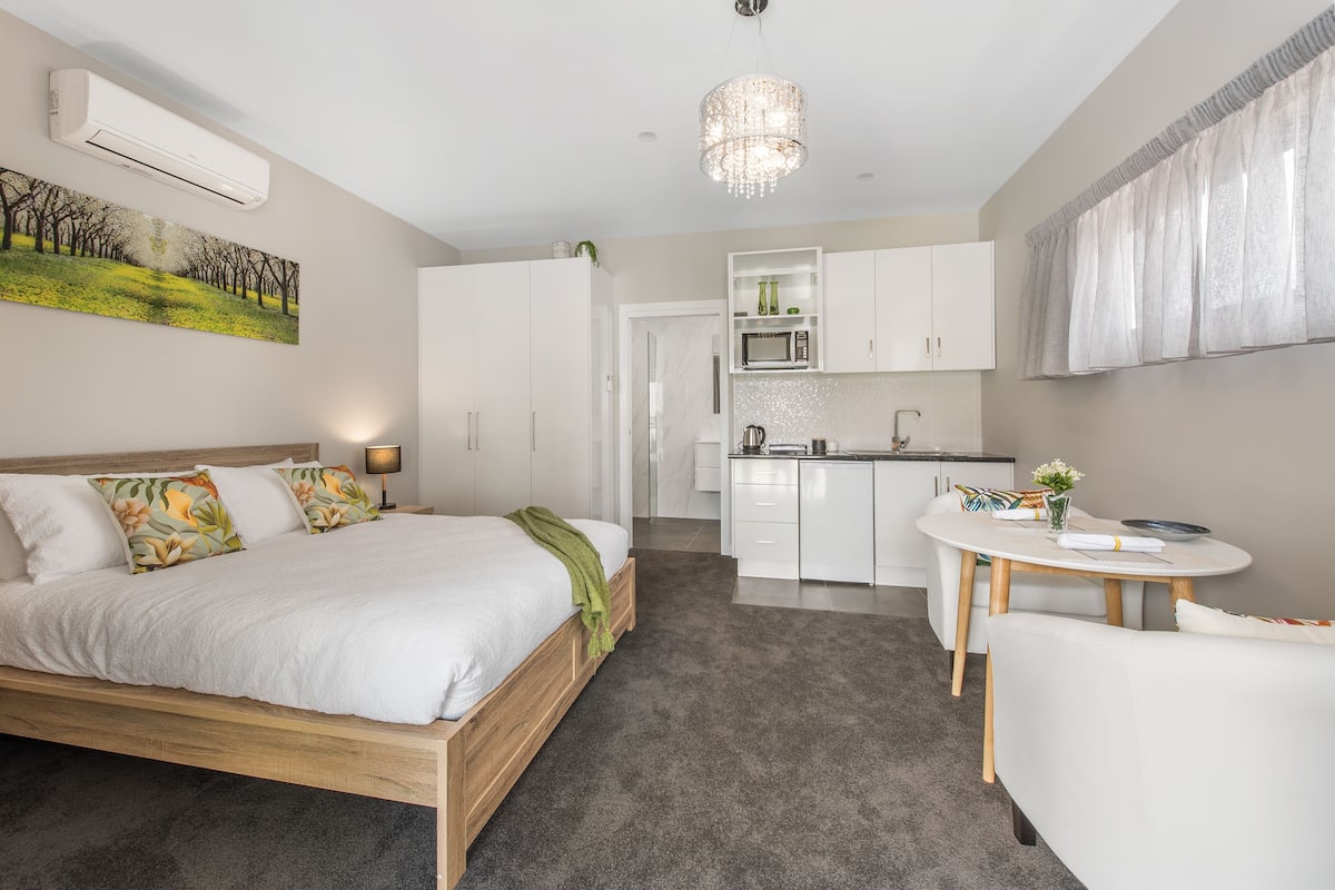 A modern bedroom with a large bed, a small dining table, and a kitchenette.