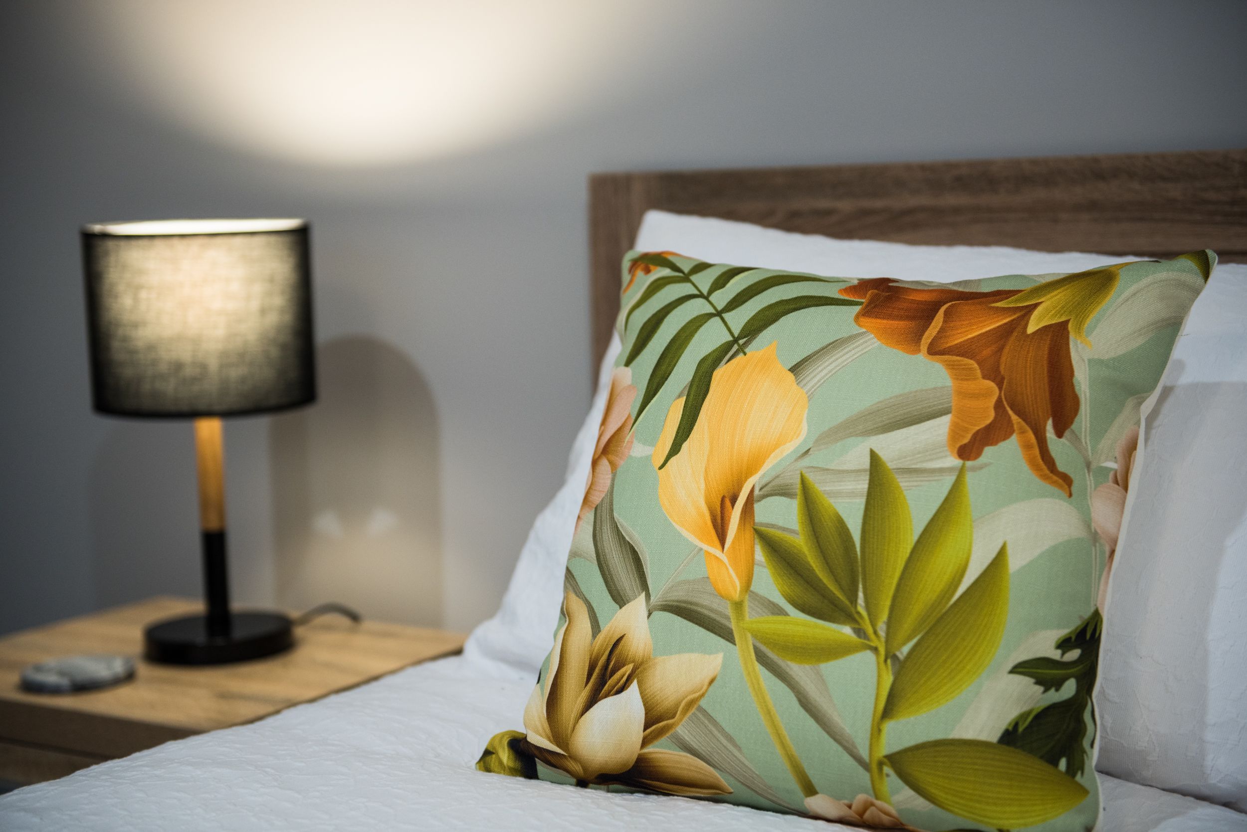 Un lit avec un oreiller à motifs floraux, une lampe de chevet et une table de nuit en bois.