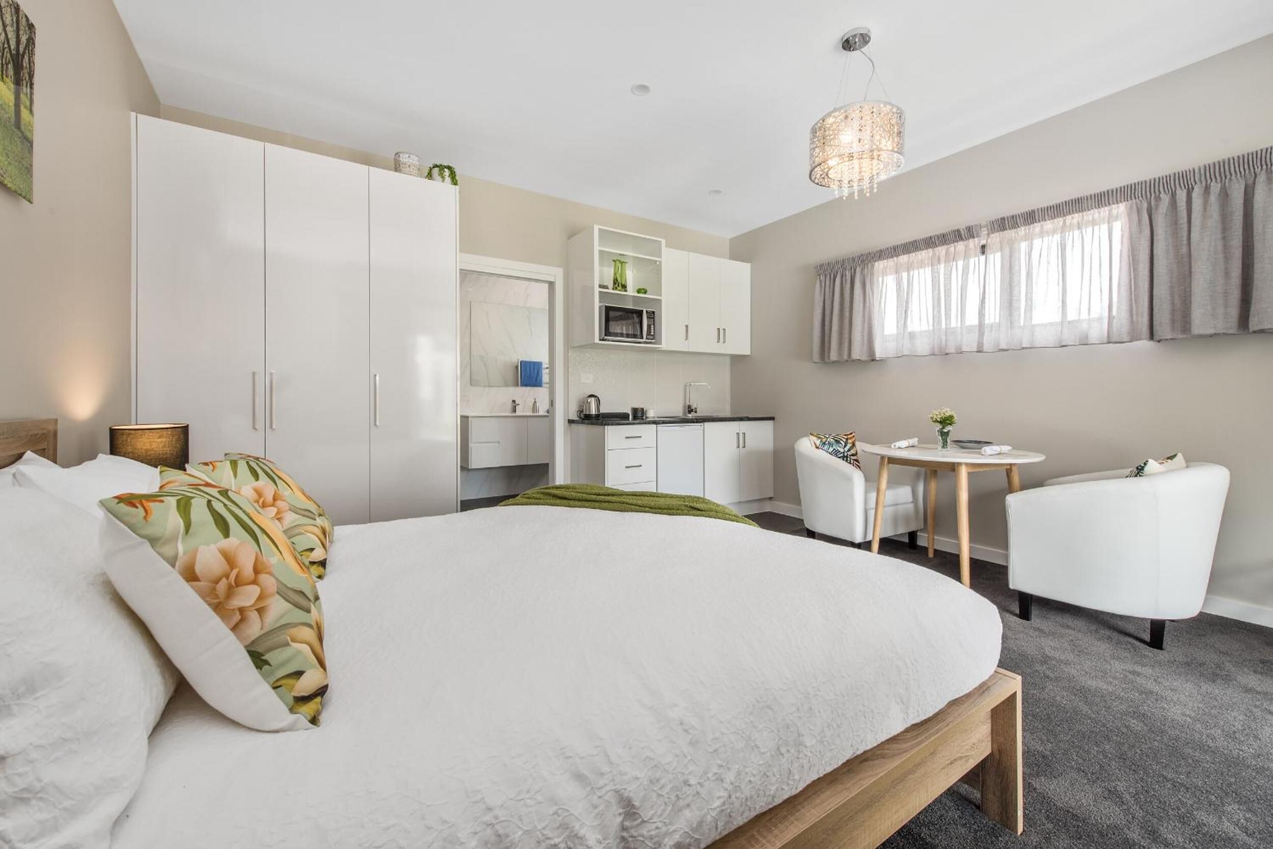 A modern bedroom with a large bed, a desk, and a kitchenette.