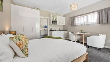 A modern bedroom with a large bed, a desk, and a kitchenette.