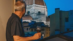 A man holding a wine glass on a balcony overlooking a historic building with a dome. - Luxury Apartment With Stunning View  (Firenze)