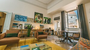 A spacious living room with a large window, a dining area, and a bookshelf filled with books and decorative items. - Luxury Apartment With Stunning View  (Firenze)