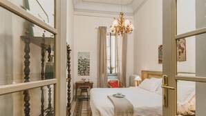 A hotel room with a large bed, a chandelier, a desk, and a view of the street through the window. - Luxury Apartment With Stunning View  (Firenze)