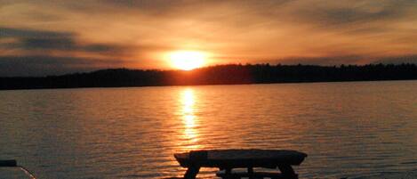 Un coucher de soleil sur un lac paisible, avec une jetée en bois et une table de pique-nique au premier plan.