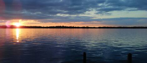 A calm body of water reflecting the sunset with a distant shoreline and overcast sky.