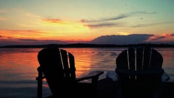 Dos sillas Adirondack mirando una puesta de sol sobre un cuerpo de agua.