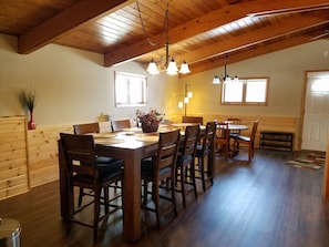 A dining area with wooden tables and chairs, a chandelier, and a window providing natural light. - A TOUCH OF COUNTRY LIVING Minutes from Madison (DeForest)