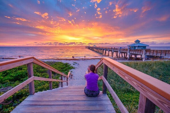 A wooden staircase leading to a beach with a pier extending into the ocean.