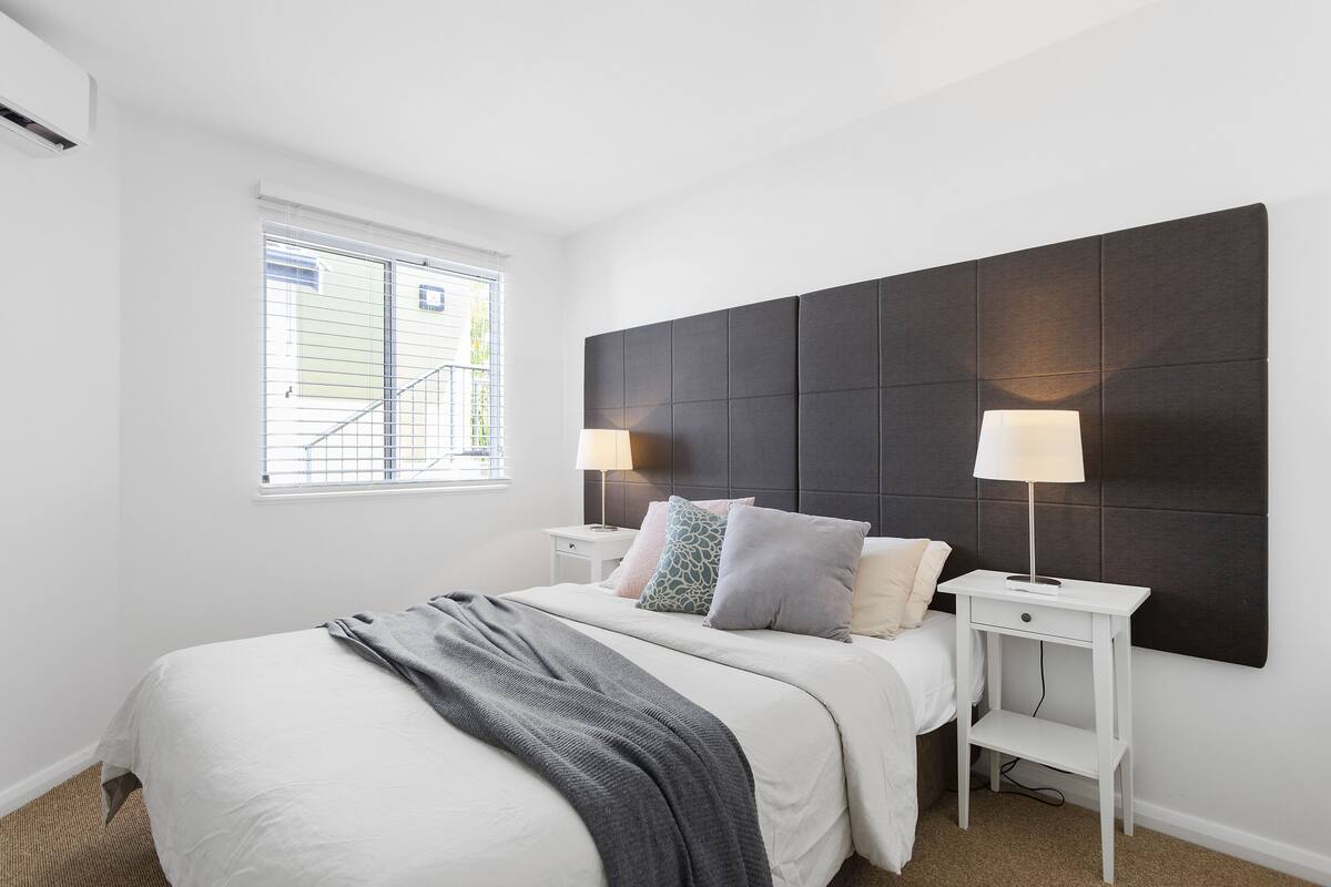 A bedroom with a bed, bedside tables, a headboard, and a window.