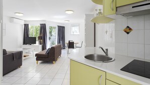 A modern kitchen with a sink, stove, and green cabinets. There is a dining area with a table and chairs, and a living room with a sofa and a TV. - Byron Getaway at Eco Beach (Byron Bay)
