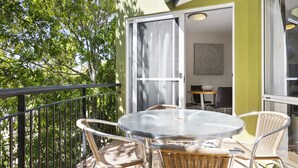 A balcony with a round table and wicker chairs, a sliding glass door, and a view of trees. - Byron Getaway at Eco Beach (Byron Bay)