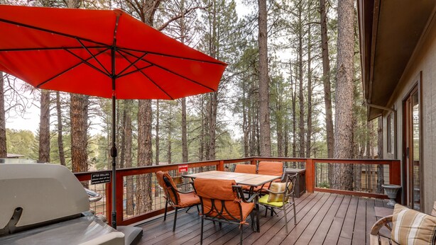 Una terraza de madera con una mesa, sillas, una parrilla y un paraguas rojo.