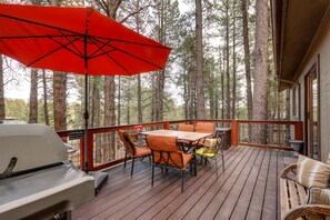 Un terrazzo in legno con tavolo, sedie, un barbecue e un ombrello rosso.