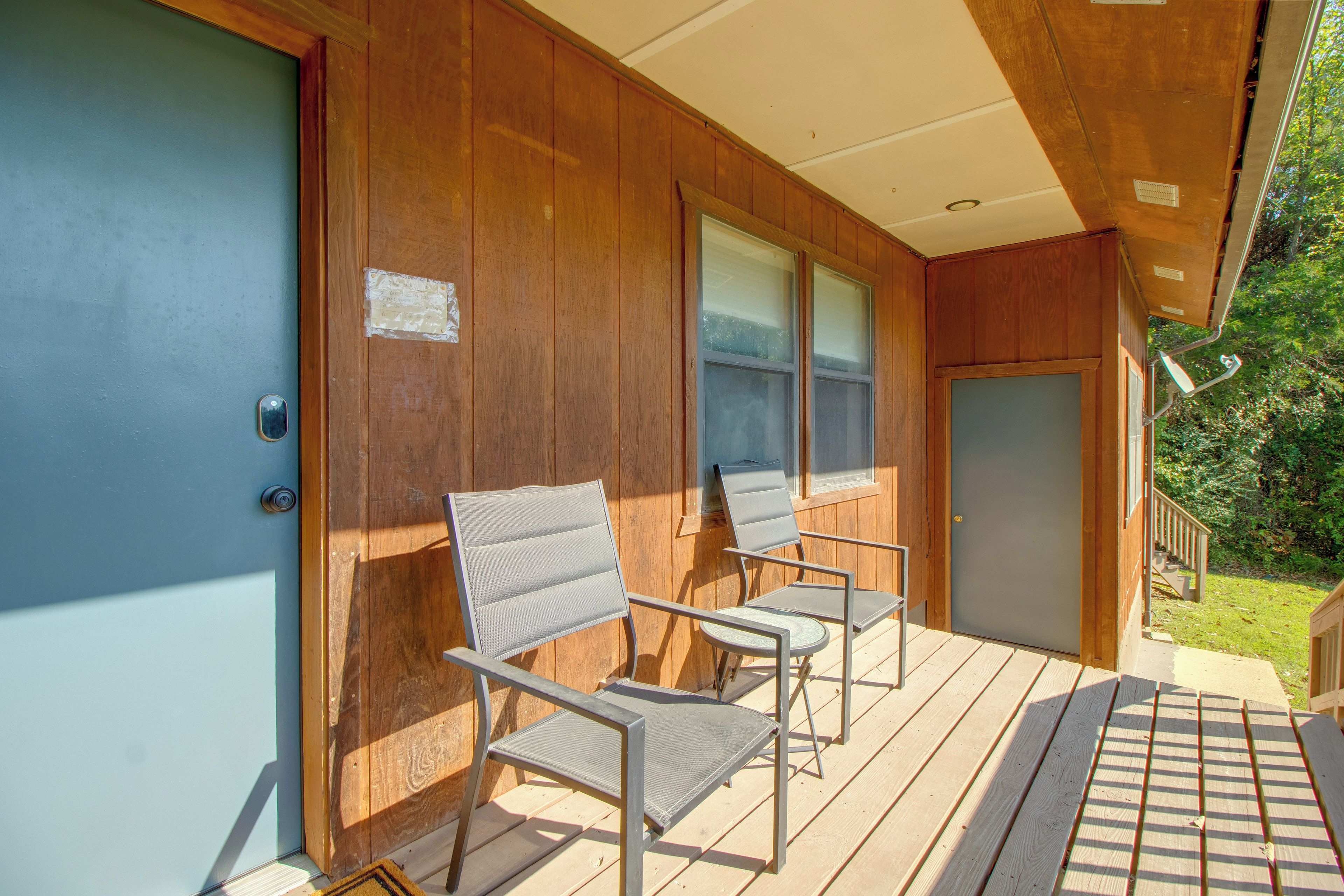 A wooden exterior with a door, two chairs, and a small table on a deck.