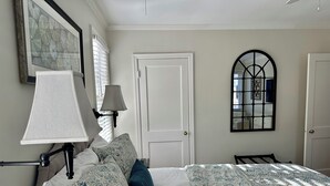 Un dormitorio ordenado con una cama, una lámpara de noche, una puerta y un espejo montado en la pared.