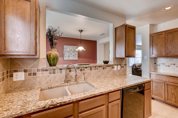 A kitchen with wooden cabinets, a granite countertop, a built-in dishwasher, and a vase with dried flowers.