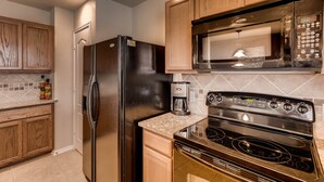 A kitchen with wooden cabinets, a stainless steel refrigerator, a microwave, and a gas stove. - BMT Grads Stay! Minutes to Lackland + Pool & Theme Parks (San Antonio)