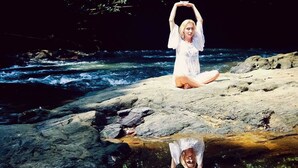 A person sitting on rocks by a river with a reflection in the water.
