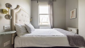 A bedroom with a bed, a nightstand, a window with curtains, and a wall-mounted light fixture. - Elegant apartment in Kensington Olympia (available for LONGER LETS) (London)