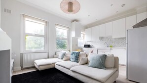 A modern living room with a sectional sofa, a black rug, and a kitchen in the background. - Elegant apartment in Kensington Olympia (available for LONGER LETS) (London)