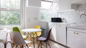 A modern kitchen with white cabinets, a microwave, a sink, and a dining area with a round table and chairs. - Elegant apartment in Kensington Olympia (available for LONGER LETS) (London)
