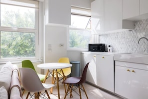 Una cocina moderna con armarios blancos, microondas, fregadero y comedor con mesa redonda y sillas.