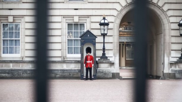 A uniformed guard standing in front of a building with a large archway and a lamp post. - Elegant apartment in Kensington Olympia (available for LONGER LETS) (London)