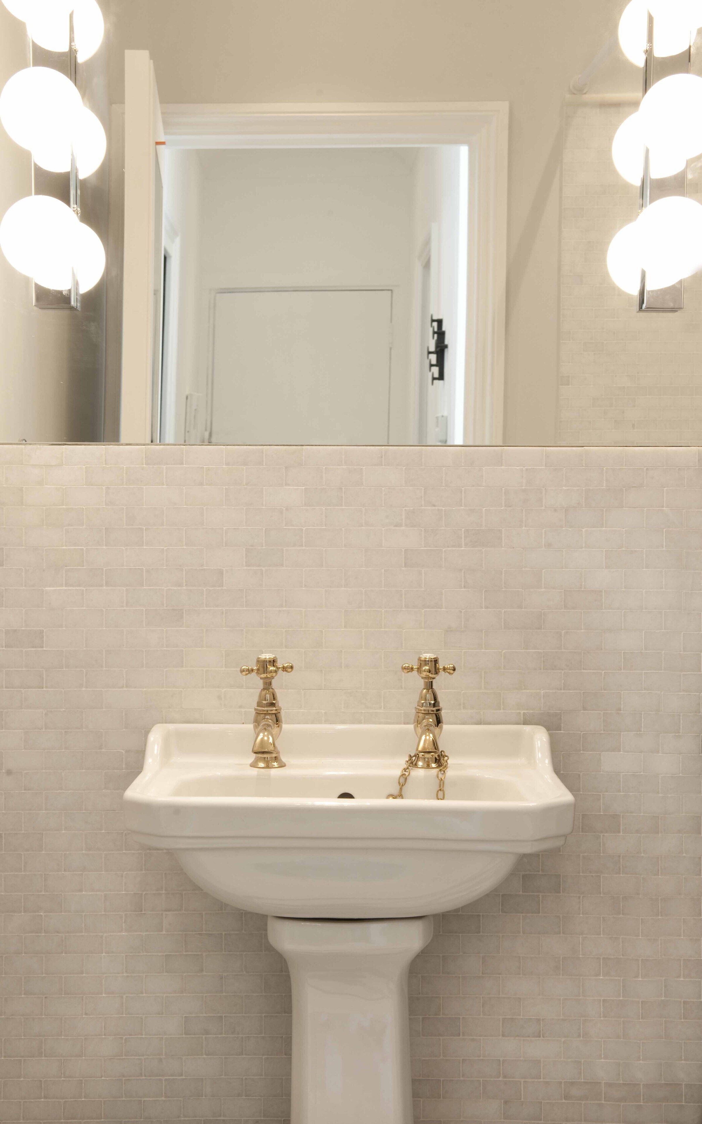 A bathroom with a white sink, gold faucets, and a mirror above it.