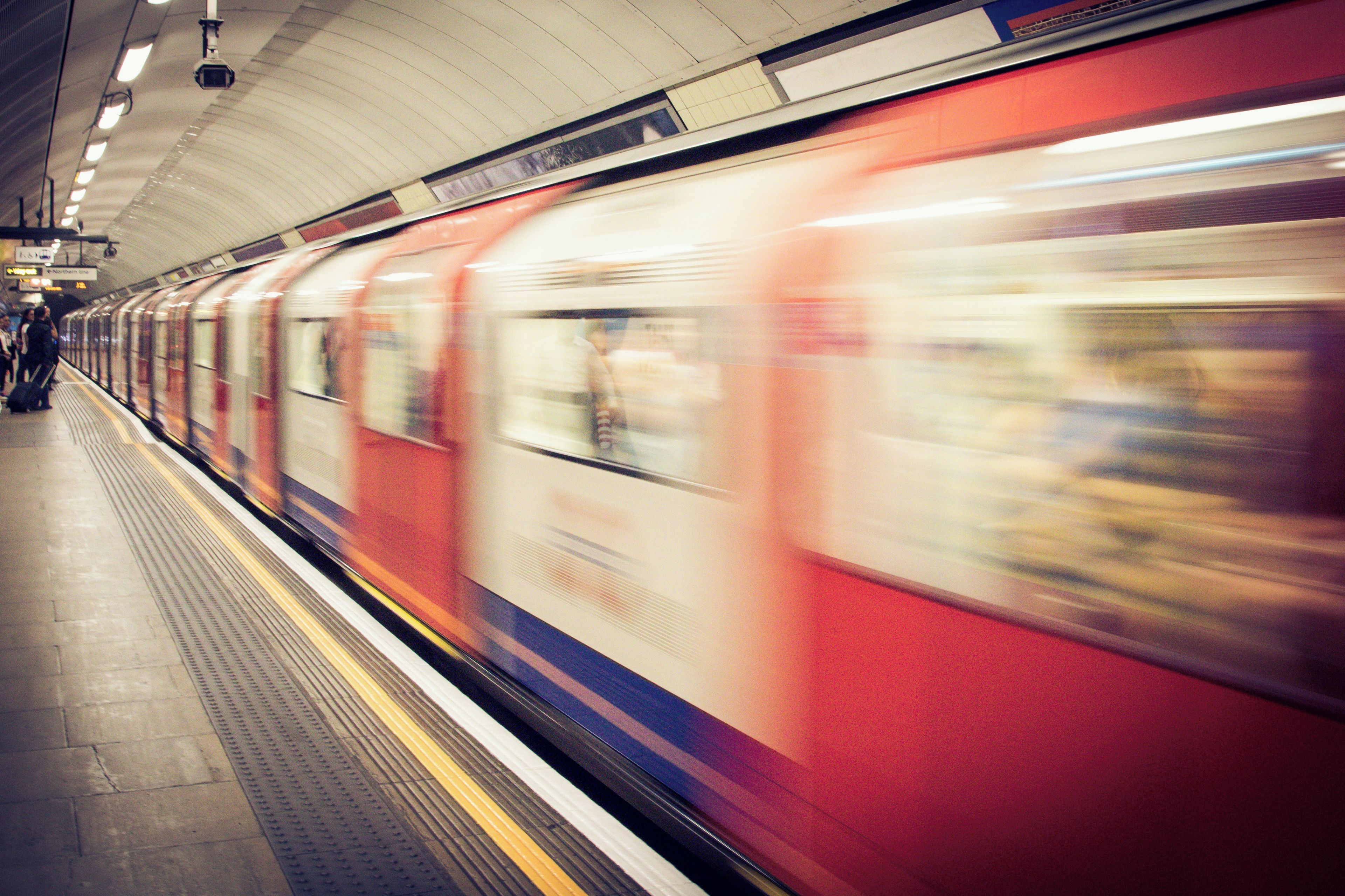 A subway train in motion, a platform with a yellow safety line, and a curved ceiling.