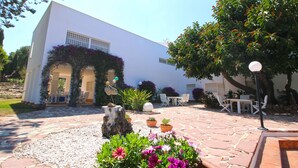 A white building with a patio area featuring a stone floor, potted plants, and outdoor furniture. - Modern Villa with pool and garden Finca La Xara (Pedreguer)