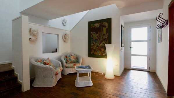 Una habitación con dos sillones de mimbre, una mesita, un cuadro y una puerta con una lámpara.