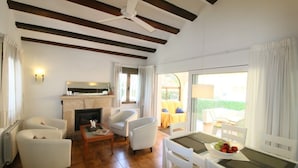 Amplia sala de estar con chimenea, muebles blancos y vistas al exterior.