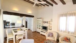 Un amplio salón con mesa de comedor, sofás blancos, televisión y estantería.