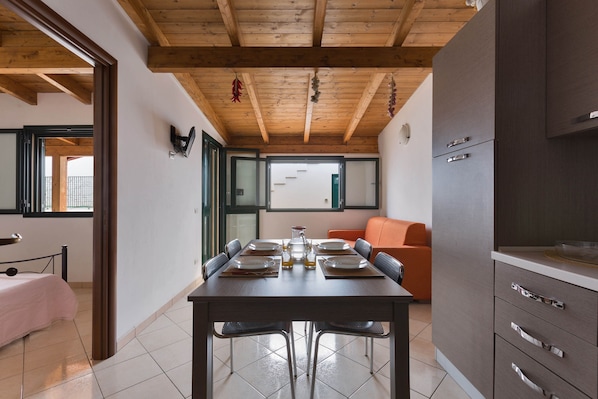 A dining area with a wooden ceiling, a table set for four, and a sofa in the background.