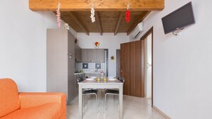 Un espace de vie compact comprenant une table à manger, des chaises, un canapé, un coin cuisine et un téléviseur fixé au mur.
