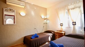 Habitación de hotel con dos camas, un espejo, luces fijadas a la pared, aire acondicionado y una ventana con cortinas.