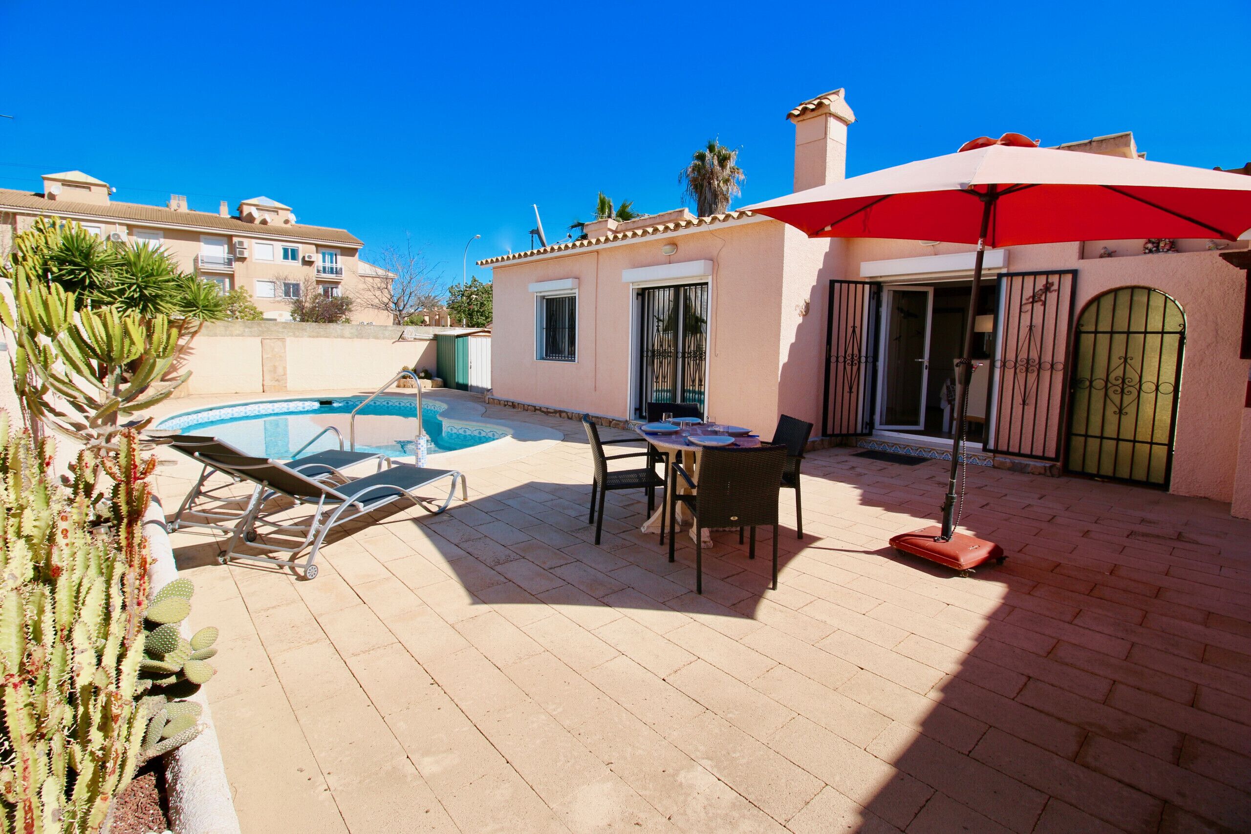 A pool area with lounge chairs, a table, and an umbrella.