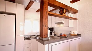 Una cocina con armarios blancos, horno empotrado, microondas y techo con vigas de madera.