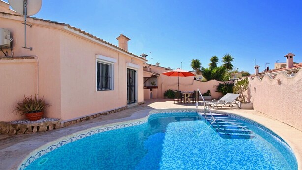 Una piscina con borde de azulejos, un área de patio con mesa y sillas, y una sombrilla roja.