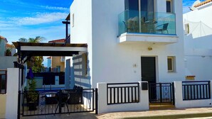 A two-story white building with a balcony, a gated entrance, and a small outdoor seating area with a grill.
