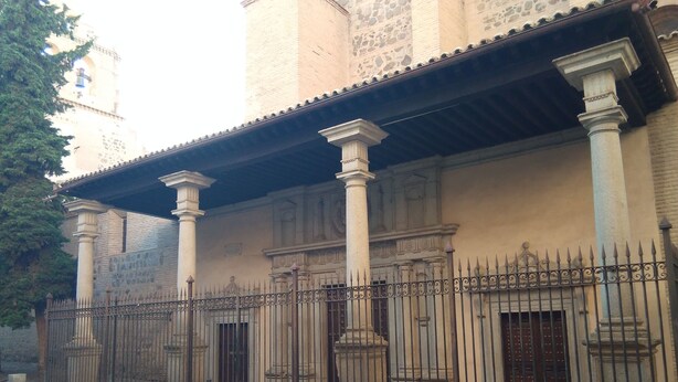 Un edificio con fachada de piedra, columnas y una verja de hierro forjado.