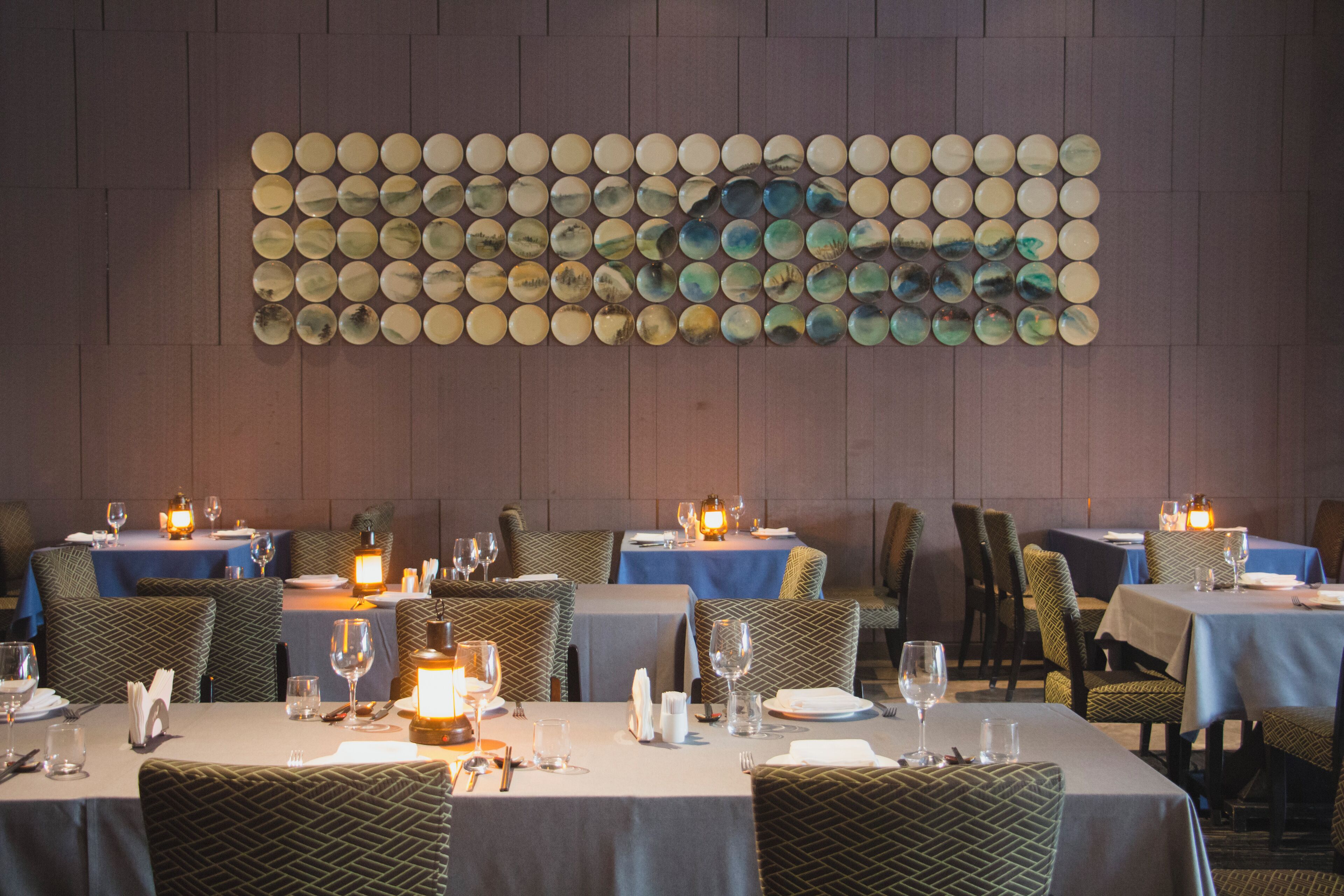 A restaurant with tables set for dining, chairs, and a wall art installation.